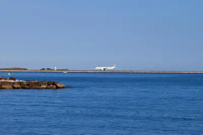 an airplane is flying over the water with a pier at The Originals City, Hôtel Galaxie, Nice Aéroport in Saint-Laurent-du-Var
