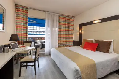 a hotel room with a bed and a desk and a table at The Originals City, Hôtel Galaxie, Nice Aéroport in Saint-Laurent-du-Var