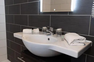 a white sink in a bathroom with black tiles at The Originals City, Hôtel Galaxie, Nice Aéroport in Saint-Laurent-du-Var