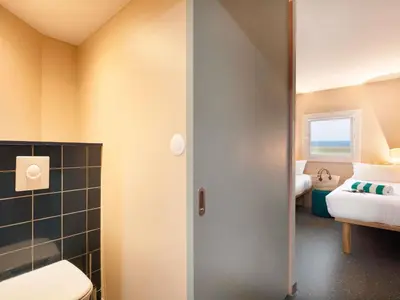 a bathroom with a toilet and a room with two beds at Greet Hotel Nice Aéroport Promenade des Anglais in Nice