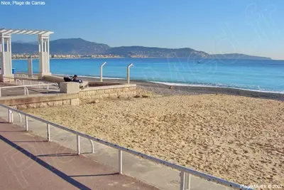 a sandy beach next to the ocean with a metal railing at Appartement F2 à 50 m de la plage in Nice
