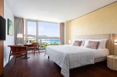 a bedroom with a bed and a desk and a large window at Le Meridien Nice in Nice