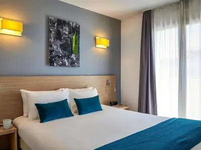 a hotel room with a large bed with blue pillows at Aparthotel Adagio Access Nice Magnan in Nice