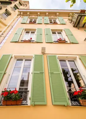 a building with green shutters and flowers on the windows at Hôtel Parisien in Nice