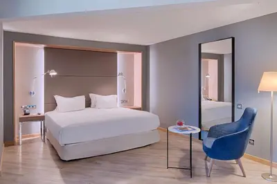 a bedroom with a white bed and a blue chair at NH Nice in Nice