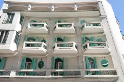 a tall white building with green and white windows at Hôtel Locarno Nice in Nice