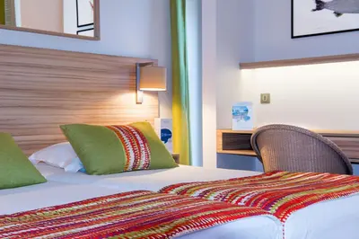 a hotel room with a bed with green and red pillows at Hôtel Vacances Bleues Delcloy in Saint-Jean-Cap-Ferrat