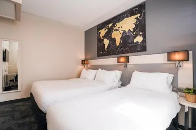 two beds in a hotel room with a map on the wall at Hôtel Univers in Nice