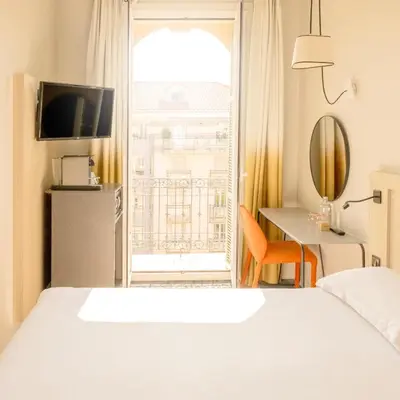 a bedroom with a bed and a large window at Hôtel Vendôme in Nice