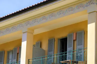 a yellow house with blue shutters and a balcony at Hotel Royal-Riviera in Saint-Jean-Cap-Ferrat