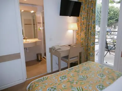 a hotel room with a desk and a bed and a bathroom at Hôtel La Flore in Villefranche-sur-Mer