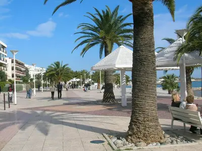 people sitting on a bench next to a beach with palm trees at Rez de villa avec beau jardin et belle vue in Saint-Laurent-du-Var