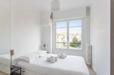 a white bedroom with a large white bed and a window at Appartement Libération - Welkeys in Nice