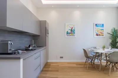 a kitchen with white cabinets and a table with chairs at Brand New 1 Bdr Place du Pin in Nice