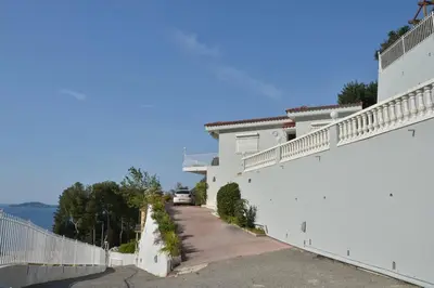 a white house with a pathway next to the water at Villa piscine Eze bord de mer à 500m de la plage in Èze