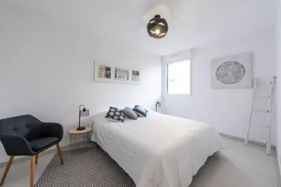 a white bedroom with a bed and a chair at Elegance in Nice