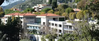 a large white building on a hill with trees at La Perle d'Eze - Aparthotel in Èze