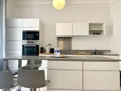 a kitchen with white cabinets and a table with chairs at ApartHotel Riviera - 2 minutes de la plage - Exceptionnel 2 chambres AC - BALCON MEYERBEER 1 in Nice
