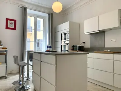 a kitchen with white cabinets and a counter with a stool at ApartHotel Riviera - 2 minutes de la plage - Exceptionnel 2 chambres AC - BALCON MEYERBEER 1 in Nice