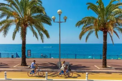 two people riding bikes on a beach with palm trees at Nice Vue Mer 50m plage Parking in Nice