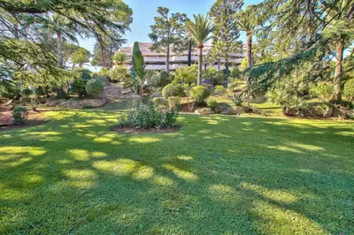 a green yard with trees and a building in the background at LE MIRAMAR Nice - Clim, Parking, Wifi et piscine in Nice