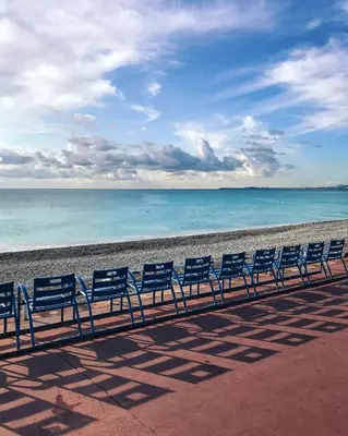 a row of blue chairs sitting on the beach at La Maioneta Vieux-Nice in Nice