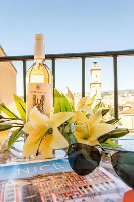 a bottle of wine and glasses on a table with flowers at Providence - ELEGANT F3, VUE INCROYABLE, BALCON,ASCENSEUR, WIFI in Nice