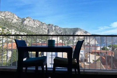 a table and chairs on a balcony with a view of the mountains at Beaulieu Sur Mer: Superbe Appart avec vue Mer in Beaulieu-sur-Mer