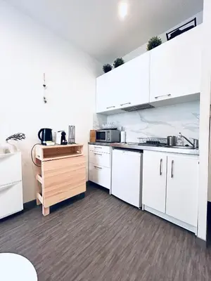 a kitchen with white cabinets and a wooden table at Studio Cocooning avec terrasse au calme Quartier Les Musiciens Mer à 7 minutes à pieds in Nice