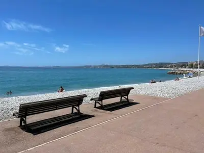 two benches sitting on a sidewalk near the beach at Appartement avec piscine privée in Cagnes-sur-Mer
