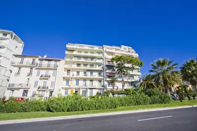 a white building with palm trees in front of a street at Holiday Vigie Promenade in Nice