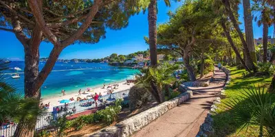 a beach with palm trees and people on the beach at Villa LE CIEL D EZE in Èze