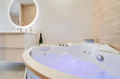 a large white tub in a bathroom with a bottle of wine at Elegant Jacuzzi Loft in Central Massena in Nice