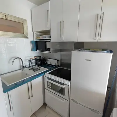 a small kitchen with white cabinets and a refrigerator at Grand studio bord de mer- accès direct aux plages in Saint-Laurent-du-Var