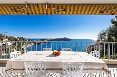 a table and chairs on a balcony with a view of the ocean at Villefranche Sur Mer:Appartement-villa, Vue mer, jardin, parking. in Villefranche-sur-Mer