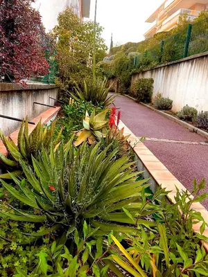a garden with some plants and a road at L Arieta - Appartement 3 pièces vue mer, parking & piscine in Nice