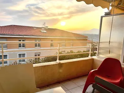 a balcony with a red chair and a view of a building at L Arieta - Appartement 3 pièces vue mer, parking & piscine in Nice