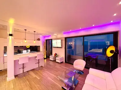 a living room with a couch and a kitchen with purple lighting at SEA VIEW TOP FLOOR - PROMENADE DES ANGLAIS in Nice