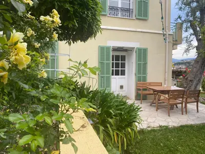 a house with green shutters and a table and chairs at Appt avec jardin et clim proche Arènes de Cimiez in Nice