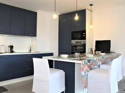 a kitchen with black cabinets and a counter with white chairs at Appartement Neuf 3 Pièces avec Terrasse et Garage, Cagnes-sur-Mer - FR-1-252A-88 in Cagnes-sur-Mer