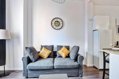 a living room with a couch and a clock on the wall at Appartement Oscarmony - Welkeys in Nice