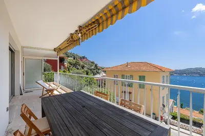 a balcony with a wooden table and chairs and the ocean at Amazing Sea View 2Bdr Swimming Pool Parking in Villefranche-sur-Mer