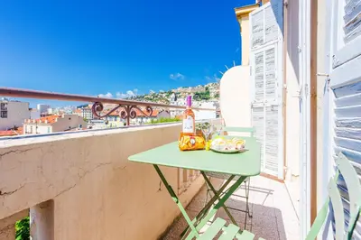 a green table on a balcony with a bottle of wine at COSY GARNIER AP4281 by Riviera Holiday Homes in Nice
