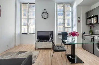 a living room with a table and a clock on the wall at Studio Famous bd Victor Hugo - city center in Nice