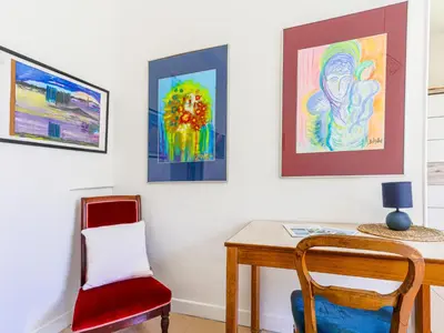 a room with a table and a chair and paintings at Apartment Hérold-2 by Interhome in Nice