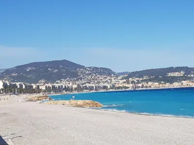 a beach with blue water and buildings and mountains at Grand studio de 30 m2 Promenade des Anglais in Nice